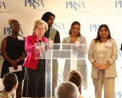 Dana Clay, in red, daughter of Ev Clay, addresses the audience while Diana La Torre, Sebastian Gonzalez, and Adelaide Doman stand in the back toward the right during the 37th Annual Ev Clay/PRSA Miami Chapter Endowment Fund Luncheon held at the Rusty Pelican on Oct. 4.